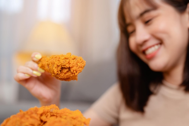 Mujer joven hambrienta comiendo comida chatarra pollo frito y papas fritas para el almuerzo ordenando la entrega, relajándose en casa de vacaciones. comida poco saludable, riesgo de obesidad.