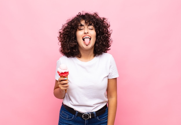 Mujer joven con un helado con actitud alegre, despreocupada y rebelde, bromeando y sacando la lengua, divirtiéndose