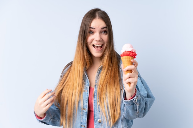 Mujer joven con un helado de cucurucho aislado en la pared azul con sorpresa y expresión facial conmocionada