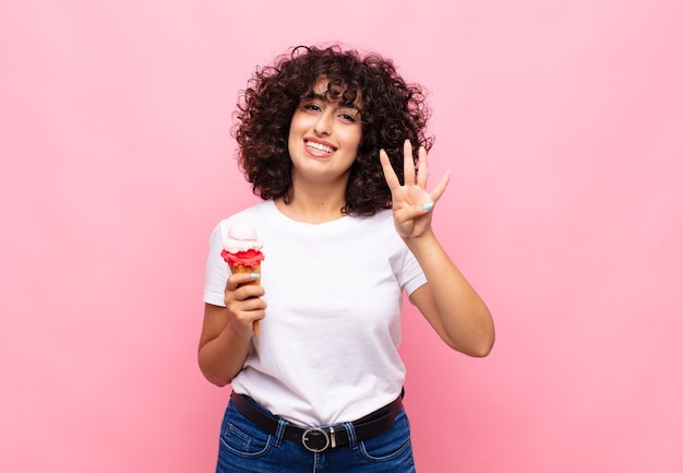 Mujer joven con un helado sonriendo y mirando amistosamente, mostrando el número cuatro o cuarto con la mano hacia adelante, contando hacia atrás