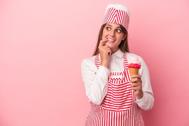 Mujer joven heladora sosteniendo helado aislado sobre fondo rosa relajado pensando en algo mirando un espacio de copia.