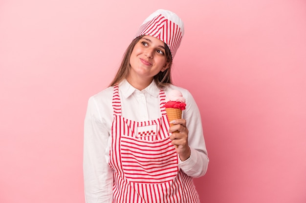 Mujer joven heladora sosteniendo helado aislado sobre fondo rosa soñando con lograr metas y propósitos