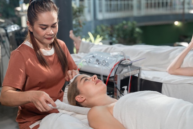 Foto mujer joven y hermosa acostada en la mesa de masaje en el salón de spa masaje facial de estética en el rostro femenino