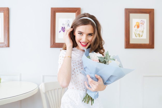 Mujer joven hermosa alegre que sostiene el ramo de flores y que mira la cámara