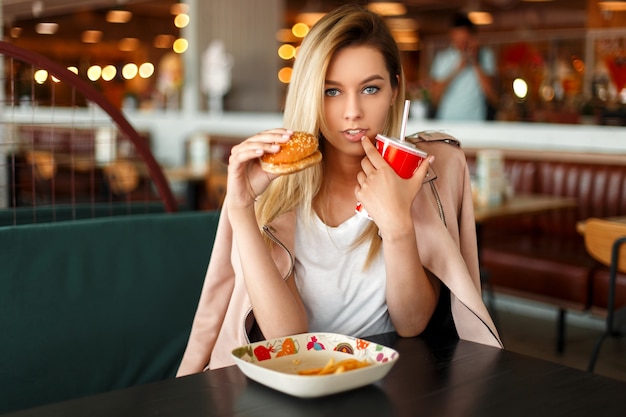 Mujer joven hermosa americana comiendo comida rápida en un restaurante