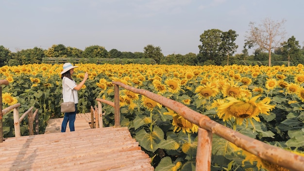 Foto mujer joven hermosa asiática caminando y tomando fotos en el fondo del paisaje del campo de girasolconcepto de viaje en temporada de verano en tailandia