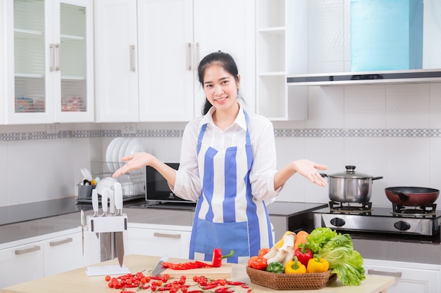 La mujer joven hermosa asiática en cocinero está mezclando talud.