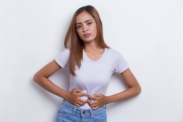 Foto mujer joven hermosa asiática enferma que tiene un dolor de estómago aislado en el fondo blanco