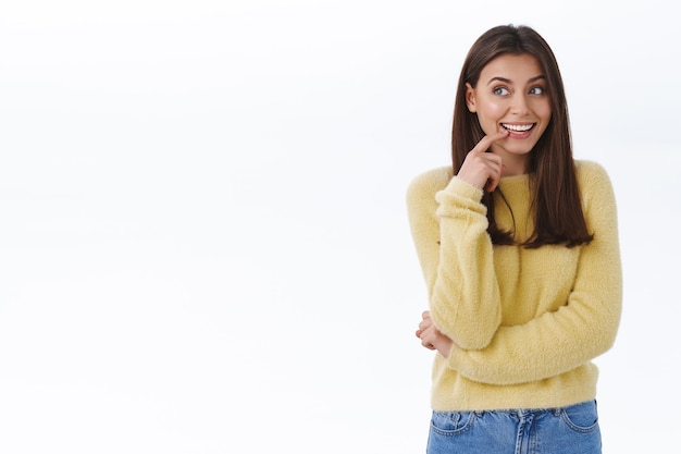 Mujer joven hermosa creativa soñadora que tiene una idea que se cruza, pensando en algo bueno, toque el labio pensativo mirando la esquina superior izquierda con una sonrisa curiosa y complacida