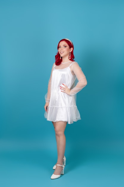 Mujer joven hermosa de cuerpo entero con el pelo rojo en vestido de malla de seda blanca y zapatos de tacón blancos