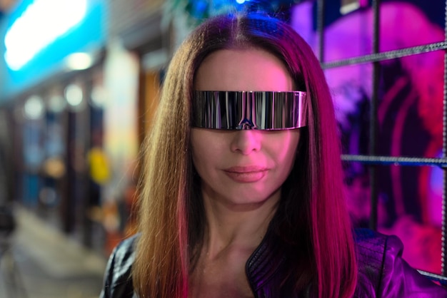 Mujer joven hermosa desenfocada en gafas cósmicas de pie junto a la colorida luz de neón en la noche con enfoque selectivo