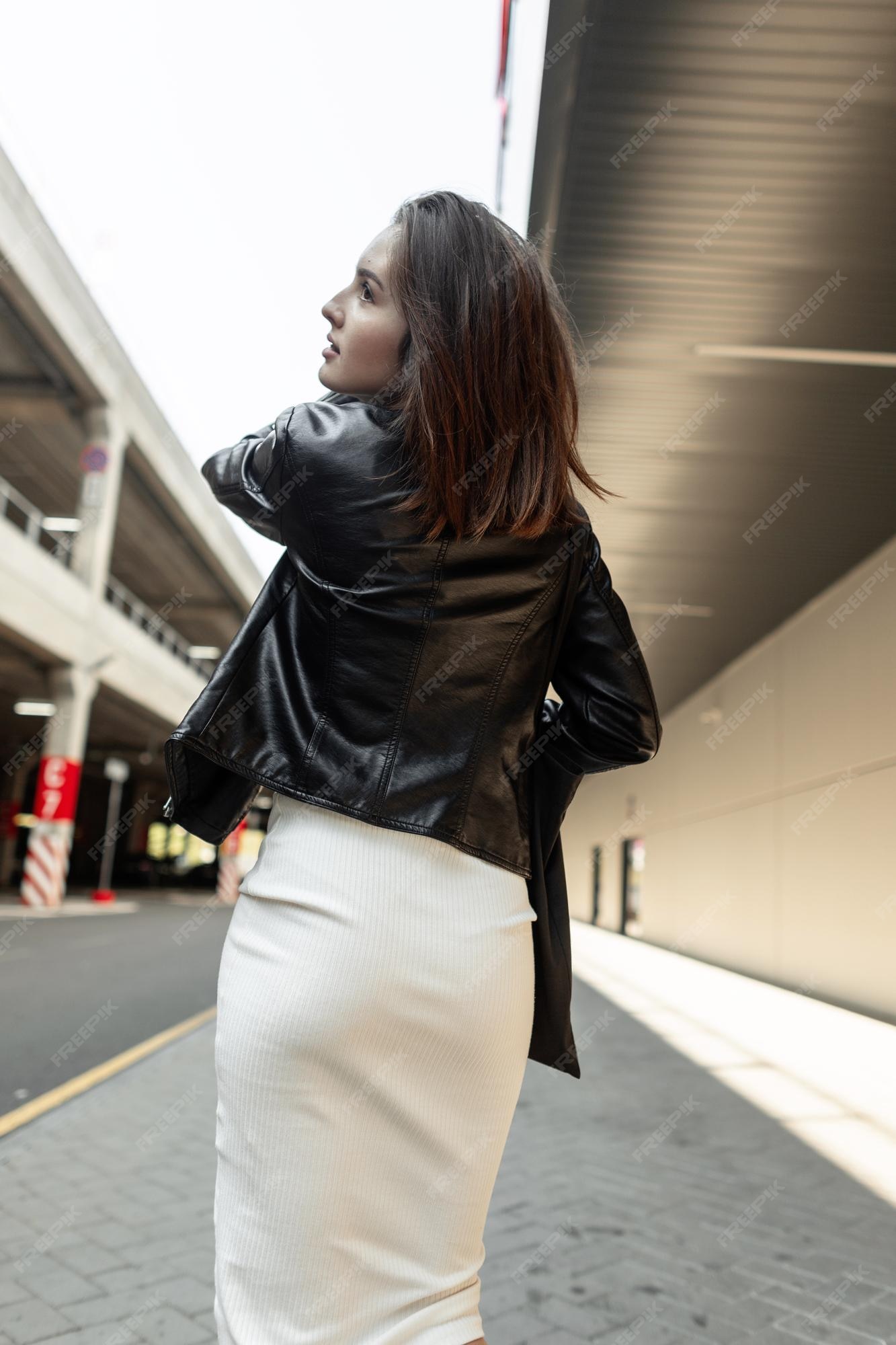 Mujer joven hermosa y elegante con peinado en una chaqueta de cuero moda y vestido con una bolsa de tela camina en la ciudad cerca de un centro comercial vista trasera