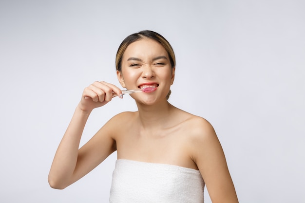 La mujer joven hermosa en el fondo aislado blanco sostiene un cepillo de dientes, asiático