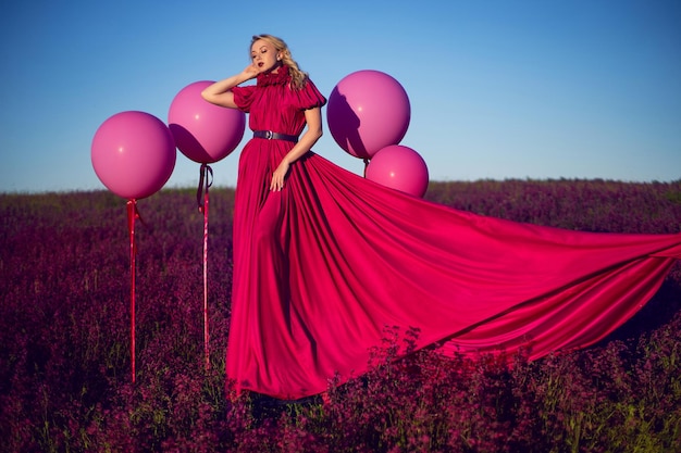 Mujer joven hermosa de moda en una escalera rosa con un vestido rosa en un campo con flores silvestres en verano al atardecer