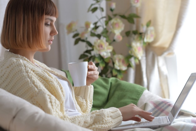 Mujer joven hermosa pelirroja bebiendo té en casa en la cama