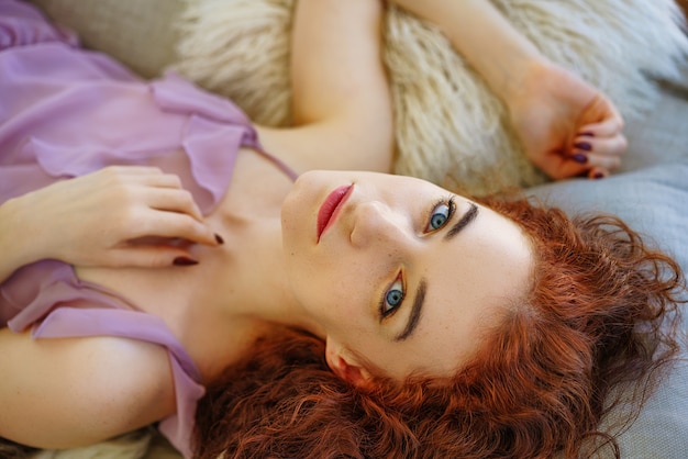 Mujer joven hermosa con el pelo rojo que miente en el sofá.