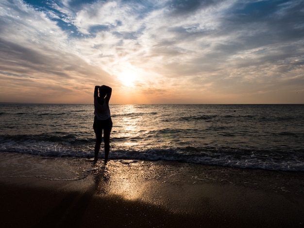 Mujer joven hacia la hermosa puesta de sol en la playa del mar. Disfrutando el momento