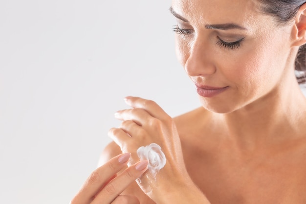 Foto mujer joven hermosa que aplica la crema en la mano aislada en blanco. concepto de cosmética y bienestar de spa de cuidado de la piel.