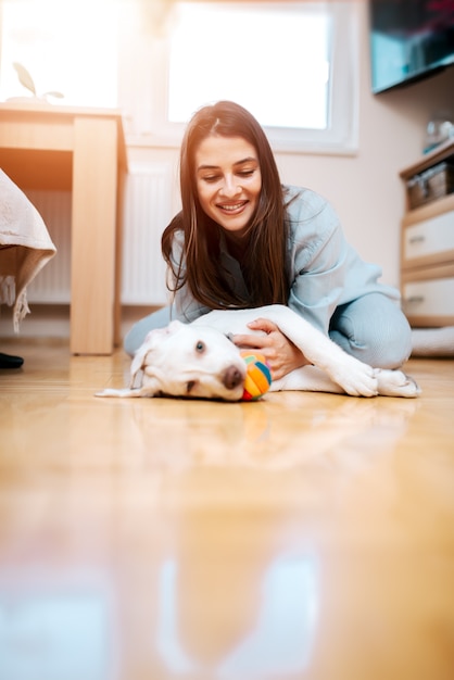 Mujer joven hermosa que juega con su perrito en casa.