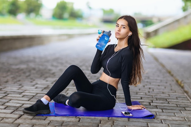 Foto mujer joven y hermosa que lleva un estilo de vida saludable escuchando música mientras está sentada en una alfombra