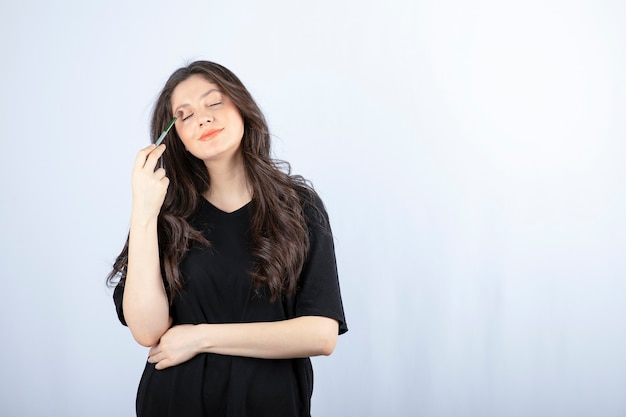 Mujer joven hermosa que pone la sombra con el cepillo cosmético sobre la pared blanca.