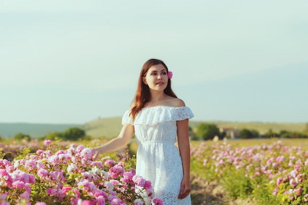 Mujer joven hermosa que presenta cerca de rosas en un jardín.