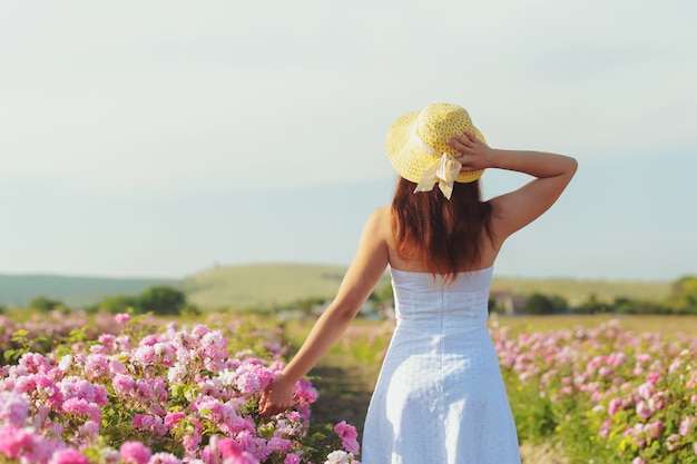 Mujer joven hermosa que presenta cerca de rosas en un jardín.