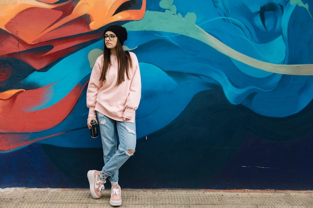 Foto la mujer joven hermosa que sostiene el aerosol puede colocarse delante de la pared colorida del graffiti