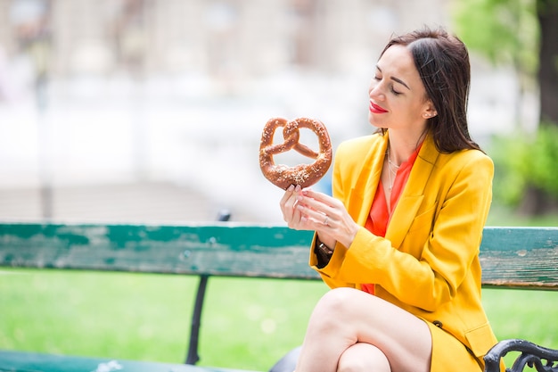 Mujer joven hermosa que sostiene el pretzel y que se relaja en parque