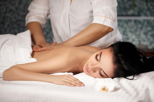 Mujer joven hermosa relajada que recibe el masaje en el salón del balneario. Tratamiento de belleza