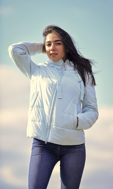 Mujer joven y hermosa sobre el fondo del cielo por encima de las nubes mirando lejos sentido de libertad futuro y éxito concepto de estilo de vida chica de moda en abrigo de otoño casual estilo otoño y primavera