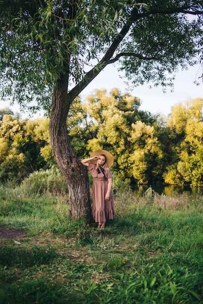 La mujer joven hermosa en un sombrero y un vestido camina en naturaleza en otoño.