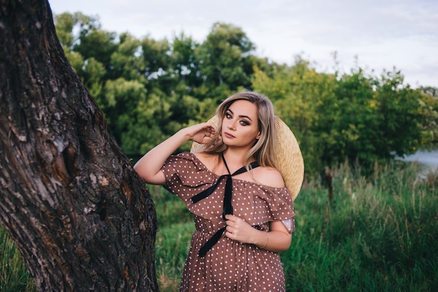 La mujer joven hermosa en un sombrero y un vestido camina en naturaleza en otoño.