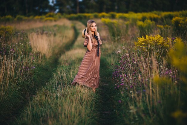 La mujer joven hermosa en un sombrero y un vestido camina en naturaleza en otoño.