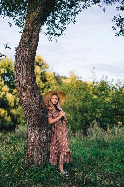 La mujer joven hermosa en un sombrero y un vestido camina en naturaleza en otoño.