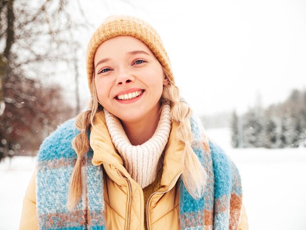 Mujer joven hermosa sonriente hipster en ropa de abrigo de moda y bufanda. Mujer despreocupada posando en la calle en el parque. Modelo puro positivo divirtiéndose en la nieve. Disfrutando de los momentos invernales