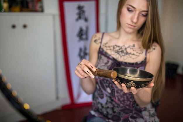 Foto mujer joven hermosa con el tatuaje de heena que juega el cuenco tibetano del canto en naturaleza