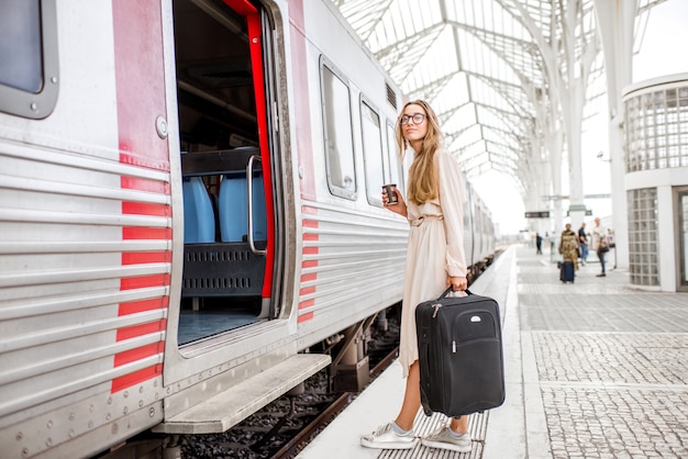 Mujer joven y hermosa con taza de café y embarque de equipaje en el tren en la estación de tren