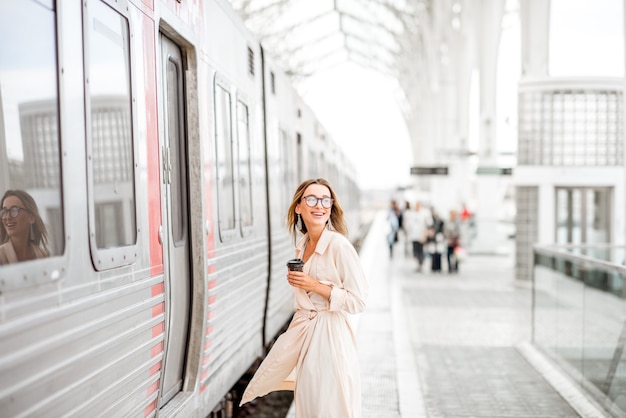 Mujer joven y hermosa con la taza de café de embarque en el tren en la moderna estación de tren