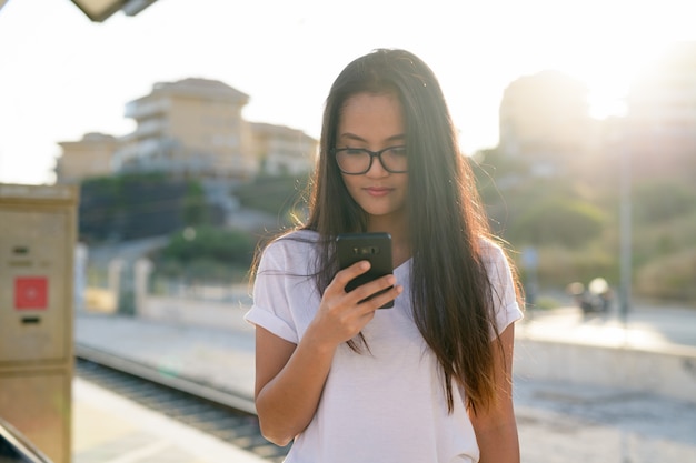 Mujer joven hermosa turista asiática con teléfono en la estación de tren