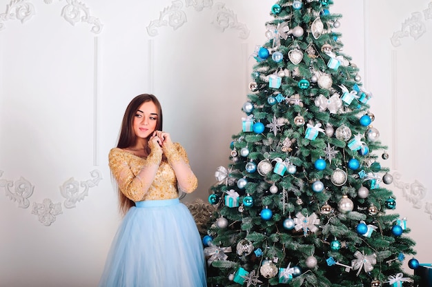 Mujer joven y hermosa con vestido largo con regalo de Navidad en las manos sentada cerca del árbol de Navidad