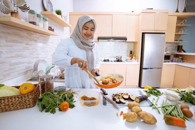 Mujer joven con hijab cocinando en su casa con cocina moderna para cenar