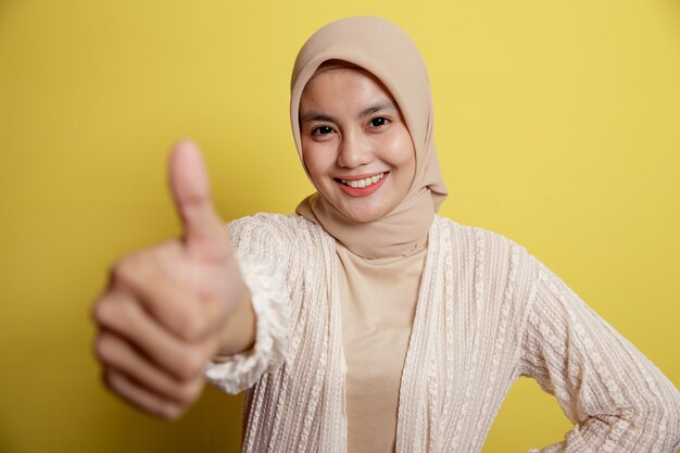 Mujer joven hijab mostrando el pulgar hacia arriba aislado en una pared amarilla