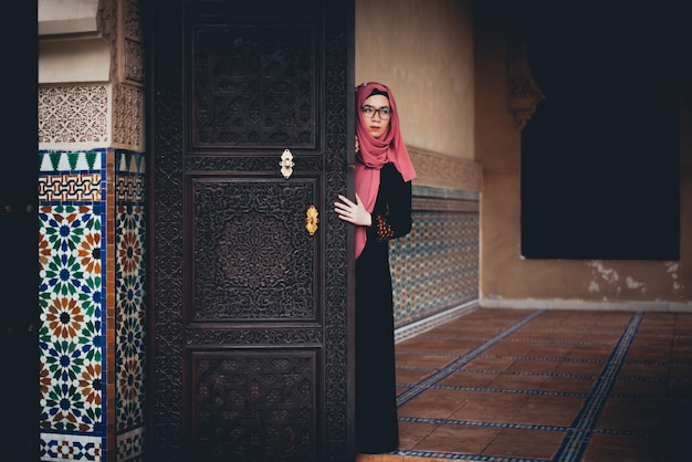 Mujer joven con hijab de pie junto a la puerta