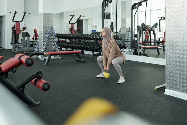 Mujer joven en hijab y ropa deportiva levantando peso pesado