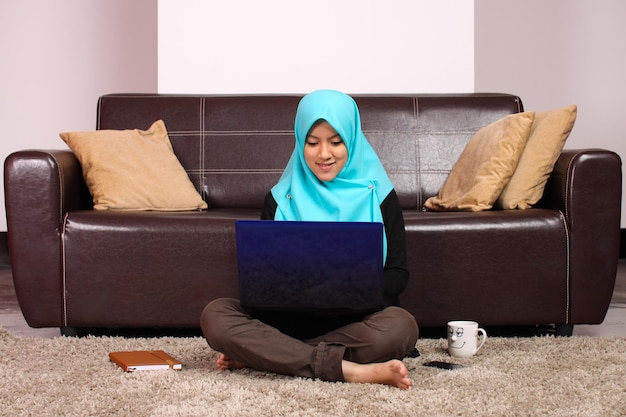 Mujer joven con hijab usando una computadora portátil en casa