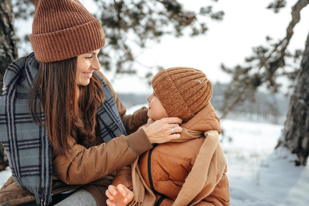 Mujer joven con un hijo en el bosque de invierno en un picnic bebe té caliente