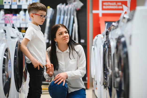 Una mujer joven con un hijo en una tienda elige una lavadora El concepto de compras