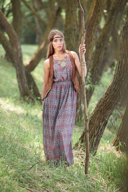 Mujer joven hippie con un bastón caminando por el bosque