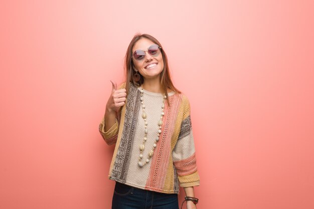 Mujer joven del hippie en el fondo rosado que sonríe y que levanta el pulgar para arriba